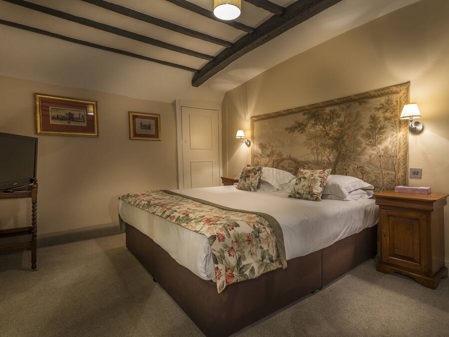 A bedroom with a large bed, wooden headboard, two wall-mounted lamps, a TV on a stand, and framed pictures on the wall.