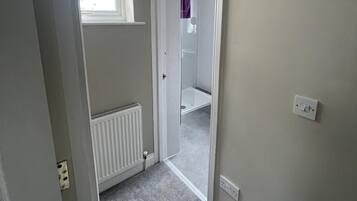 A narrow hallway with a radiator, a white door leading to a bathroom, and a ceiling light fixture.