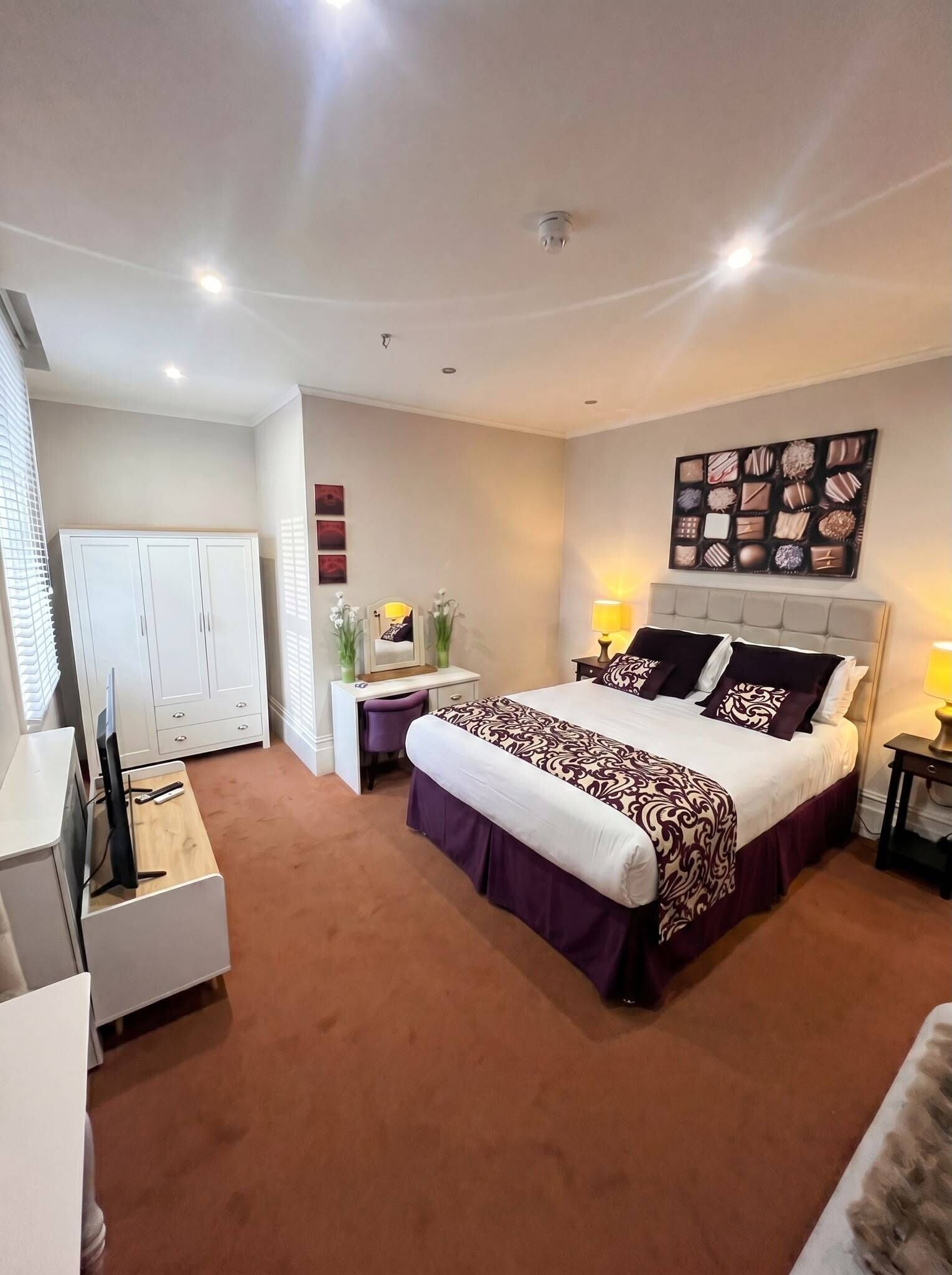 A bedroom with a bed, bedside tables, a desk, a wardrobe, and a wall art piece.