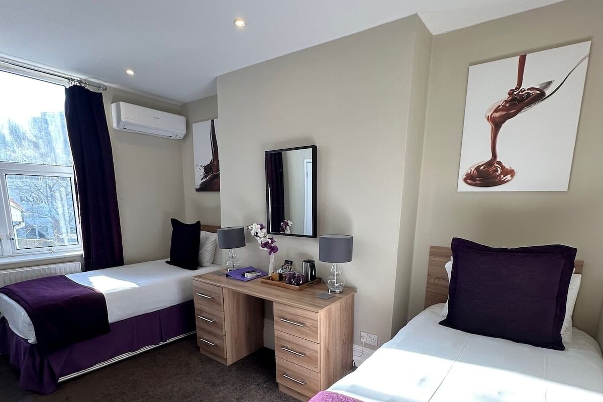 Quarto de hotel com duas camas, uma escrivaninha, um espelho e uma janela com cortinas.