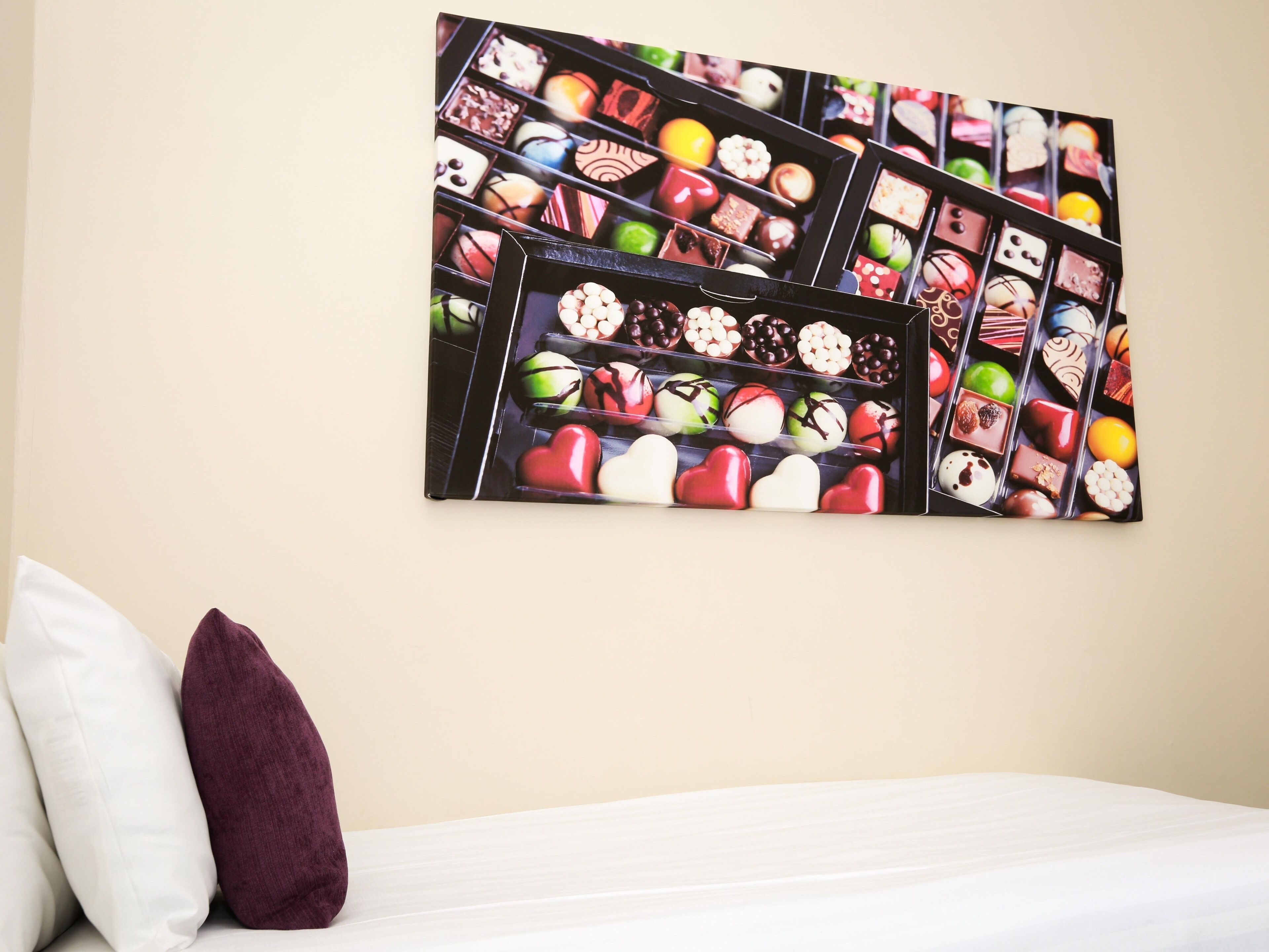 Ein Hotelzimmer mit Bett, Kissen und einer Wanddekoration mit verschiedenen Schokoladensorten.