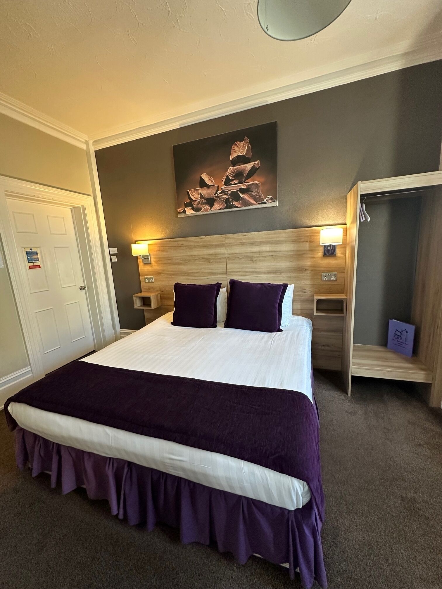 Une chambre à coucher bien aménagée, avec un grand lit, deux tables de chevet, une œuvre d’art accrochée au mur et un placard intégré.