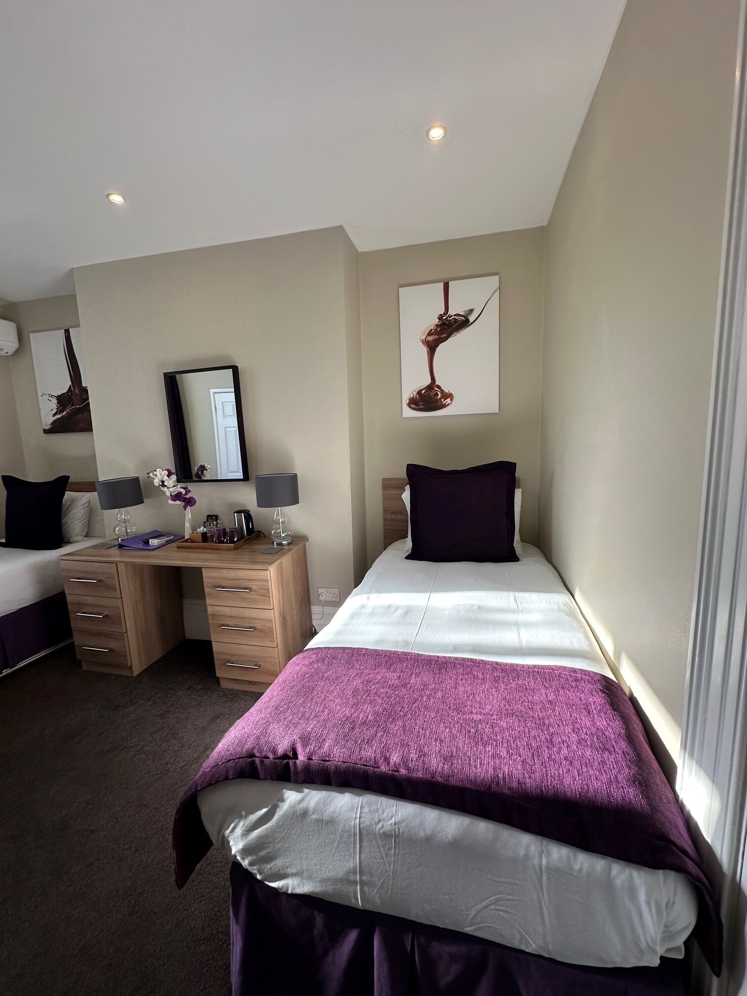 A hotel room with two beds, a desk, a dresser, a mirror, and artwork on the walls.