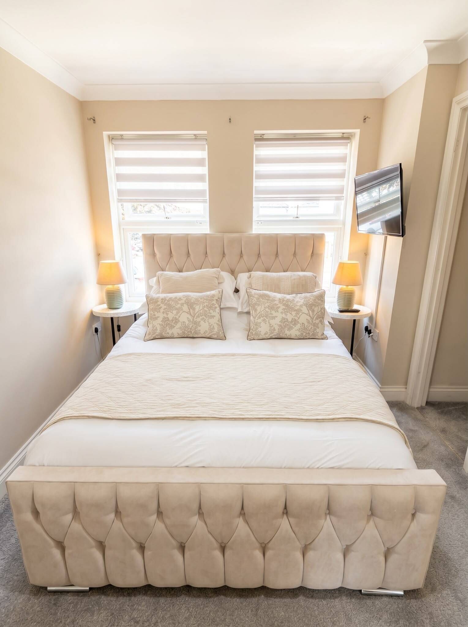 Un dormitorio con una cama grande, dos mesitas de noche con lámparas, un televisor de pantalla plana en la pared y una ventana con persianas.