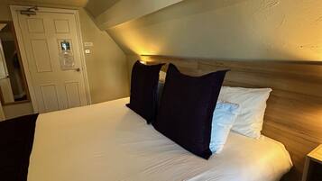 A large bed with a wooden headboard, a bedside table, and a door with a security lock.