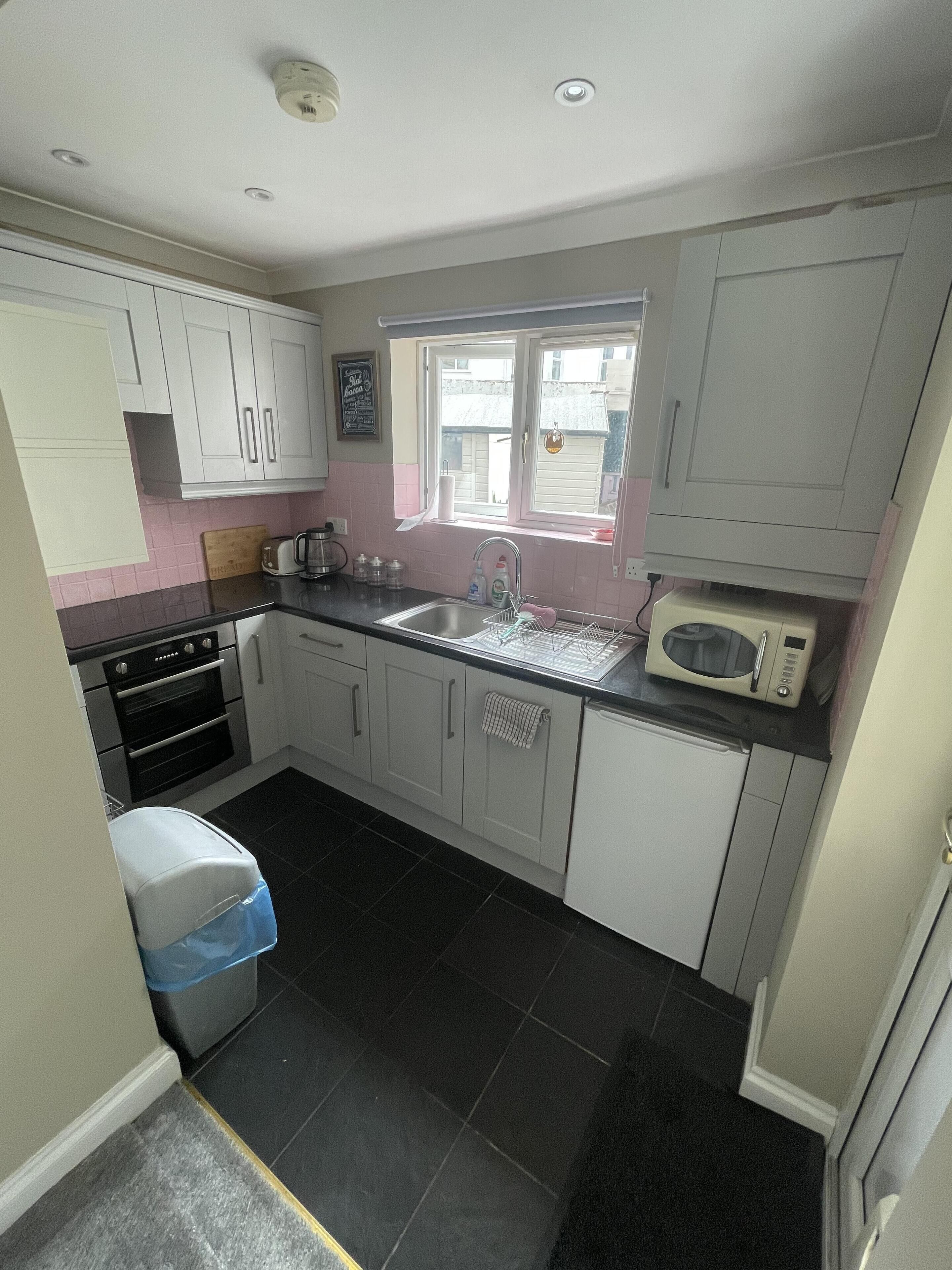 A compact kitchen with white cabinets, a black countertop, a microwave, a sink, and a window.