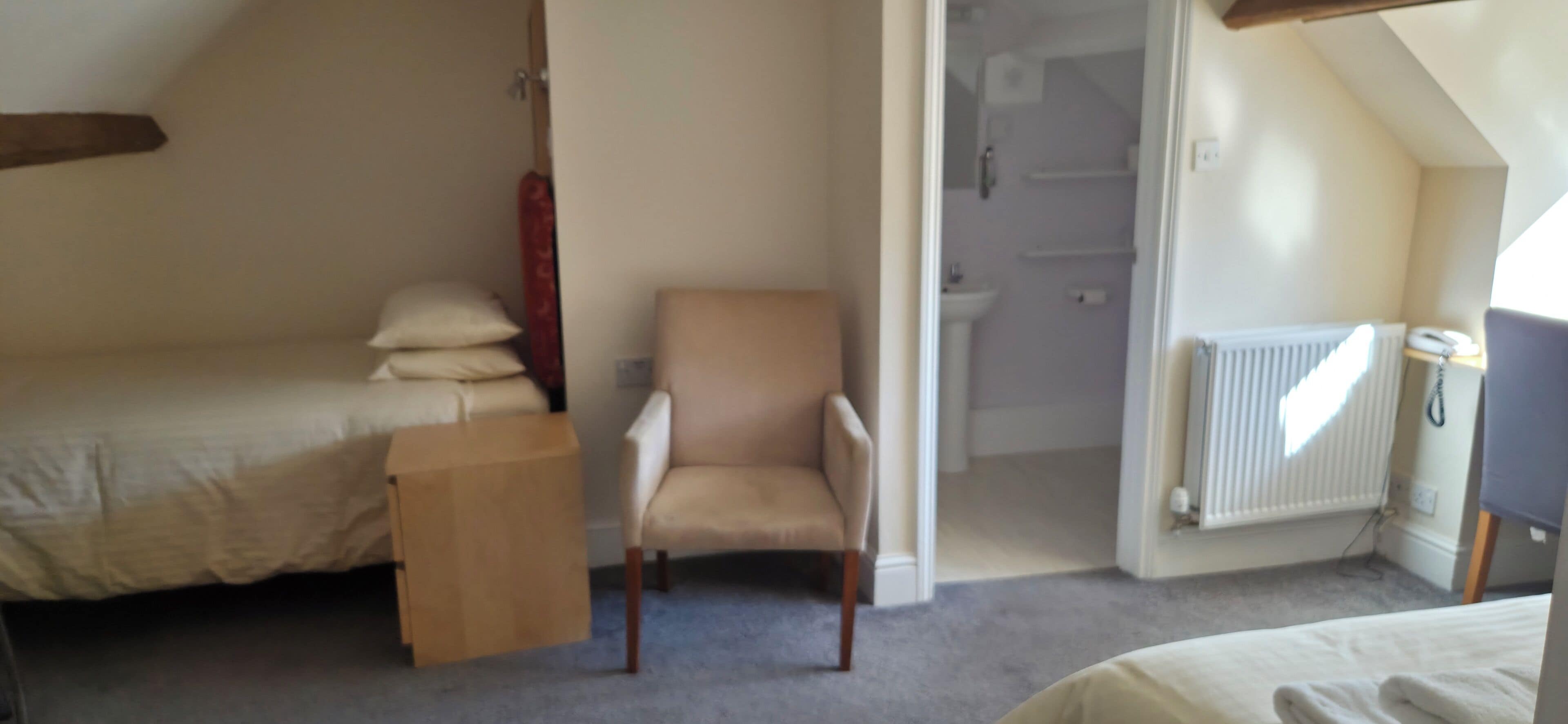 A bedroom with a bed, a chair, a small table, and a radiator.