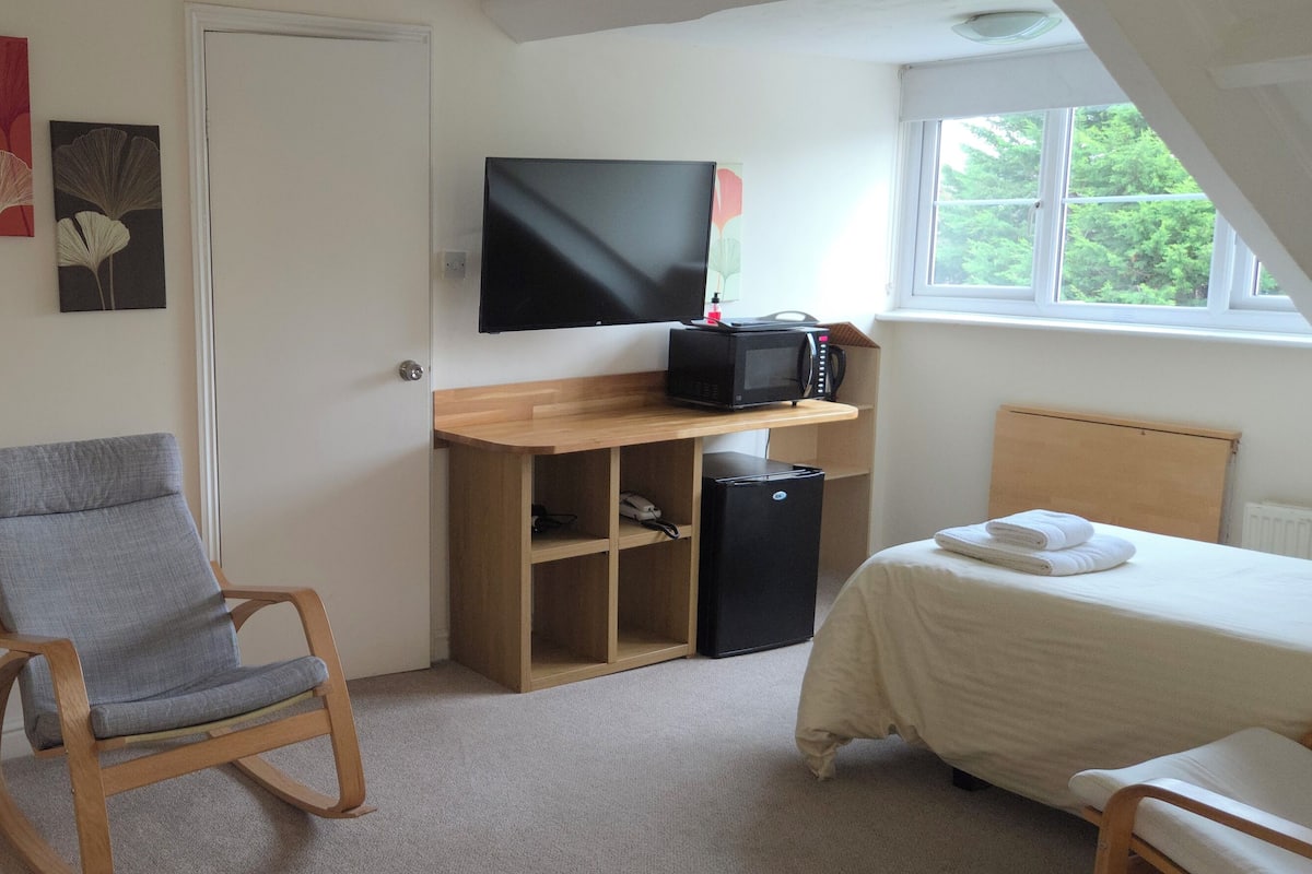 A bedroom with a bed, a desk with a computer, a chair, a lamp, and artwork on the wall.