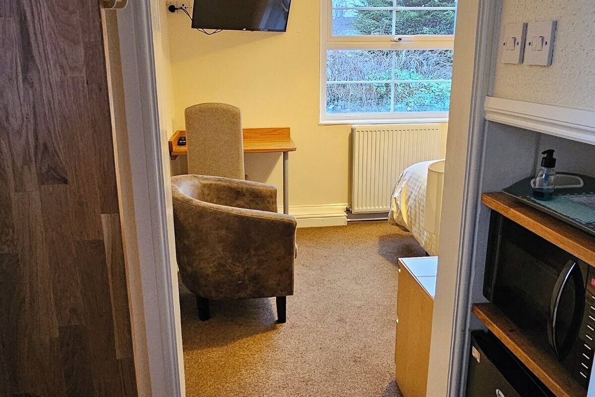A narrow hallway leading to a living area with a sofa, a television mounted on the wall, and a window with a view of greenery.