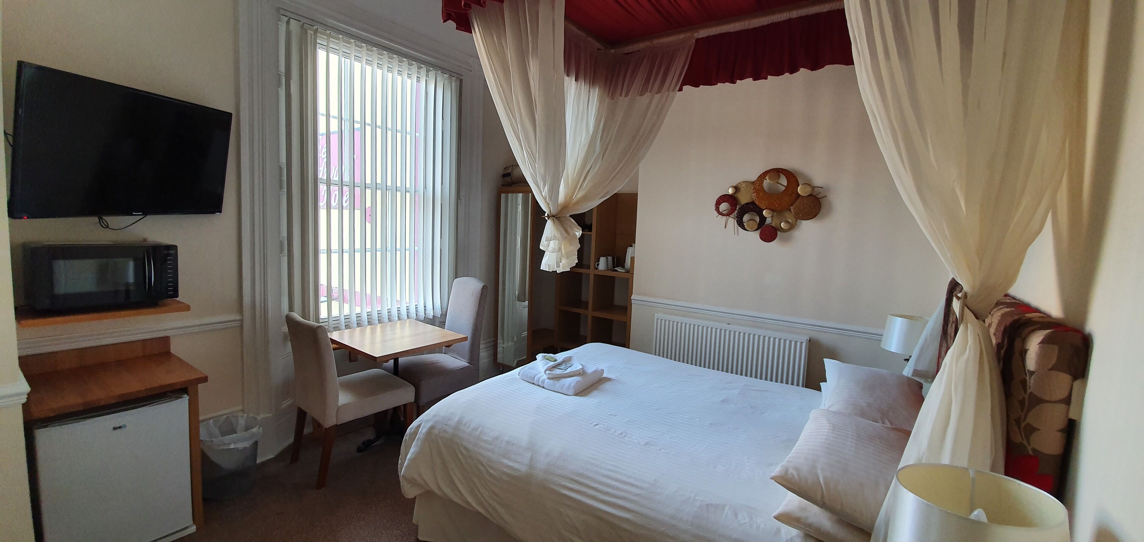 A hotel room with a bed, a desk, a television, and a window with curtains.