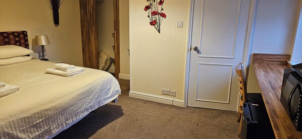 A hotel room with a bed, a nightstand with a lamp, a wooden dresser, and a microwave. - The Edward Hotel (Gloucester)