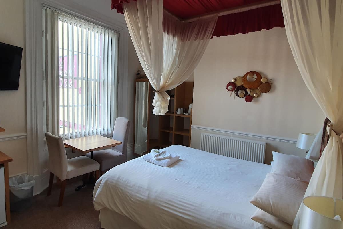 A hotel room with a bed, a desk, a television, and a window with curtains.