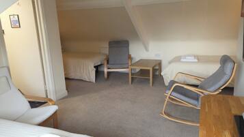 A compact room with a bunk bed, a single chair, a small table, and a bed with a pillow and blanket.
