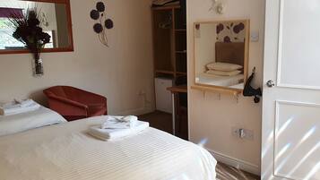 A hotel room with a bed, a red chair, a wardrobe, a mirror, and a small table.