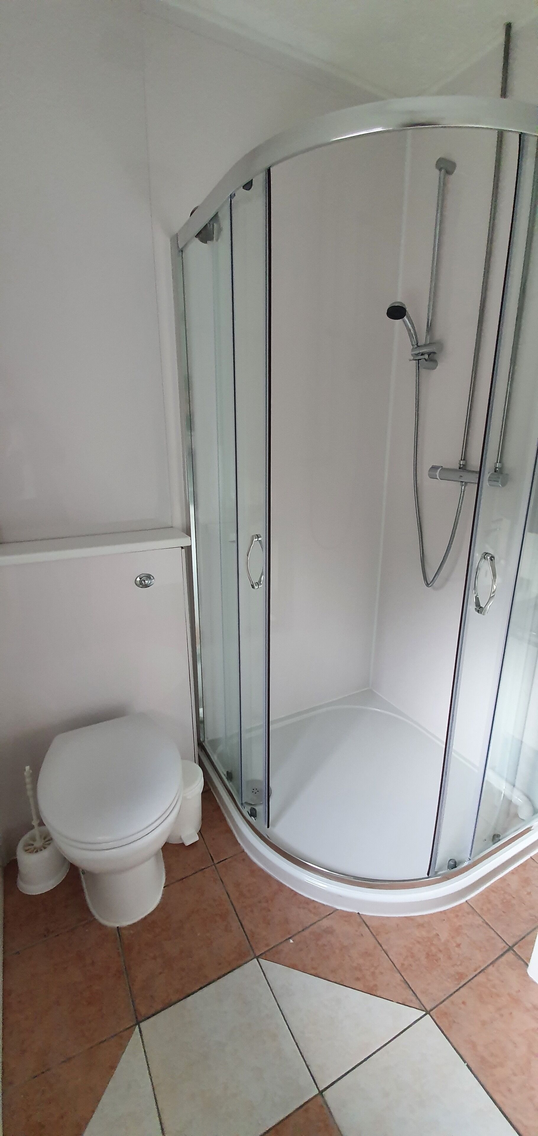 A bathroom with a glass-enclosed shower, a toilet, and a tiled floor.
