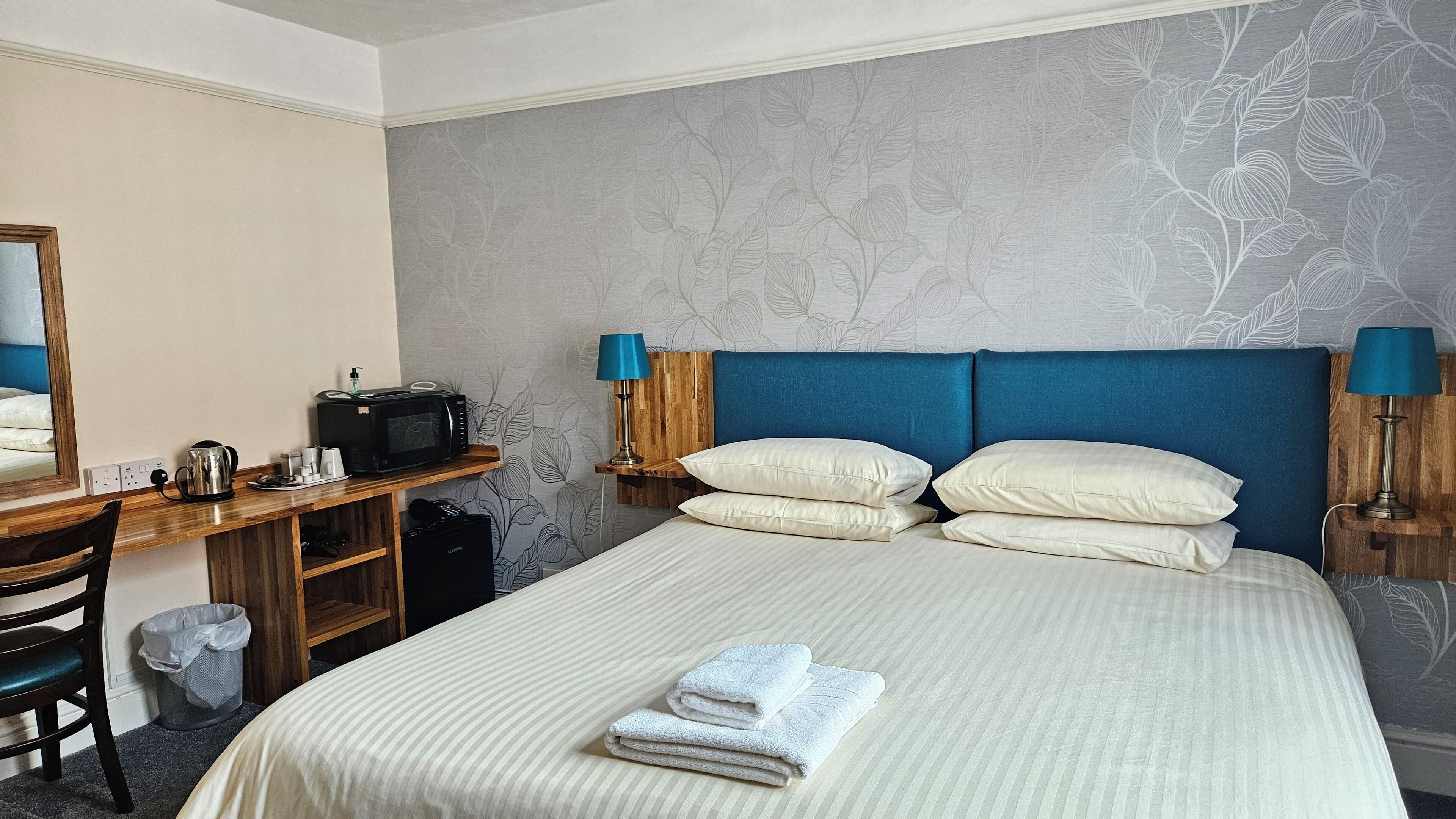 A hotel room with a bed, a desk with a microwave, a chair, and a trash bin.