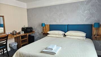 A hotel room with a bed, a desk with a microwave, a chair, and a trash bin.