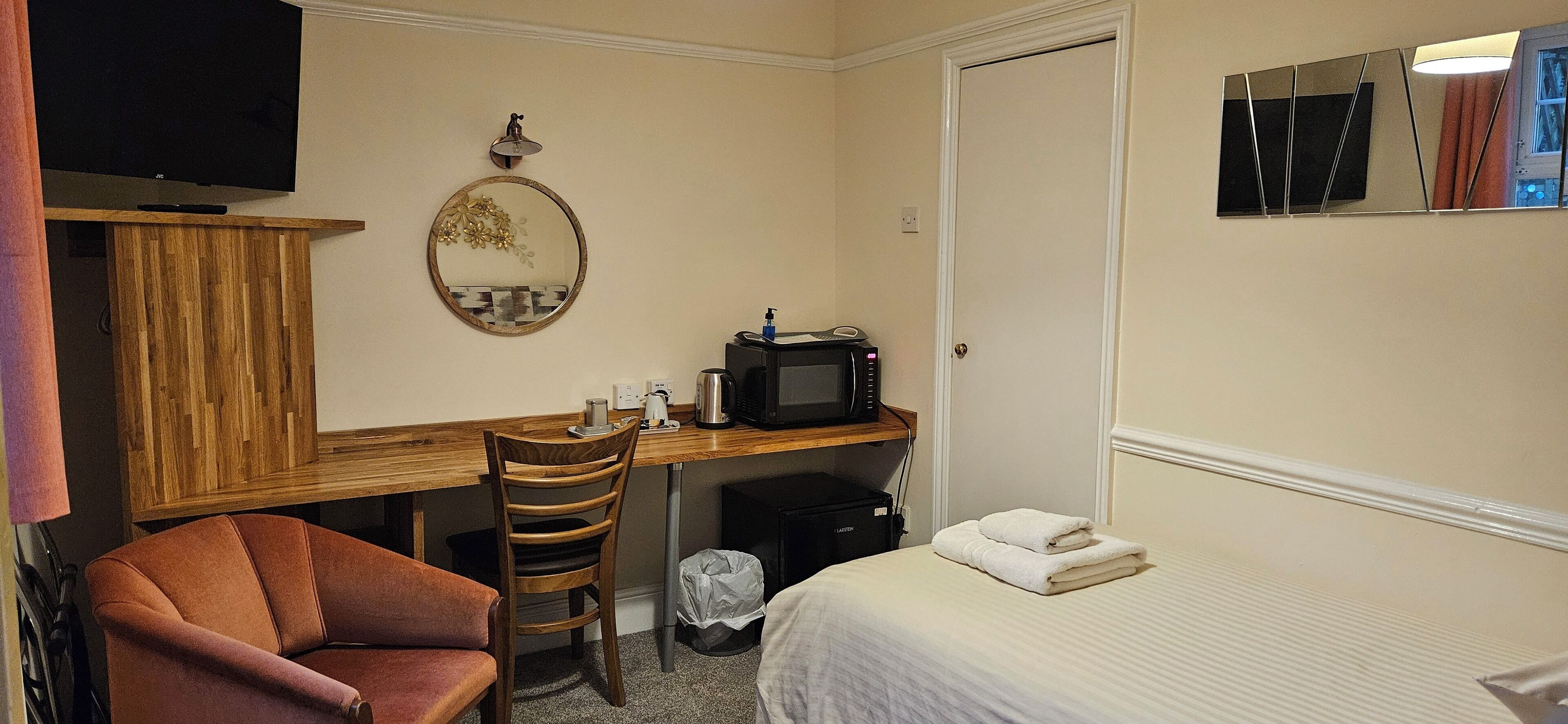 A hotel room with a wooden desk, a chair, a bed, a TV, a microwave, and a mirror.