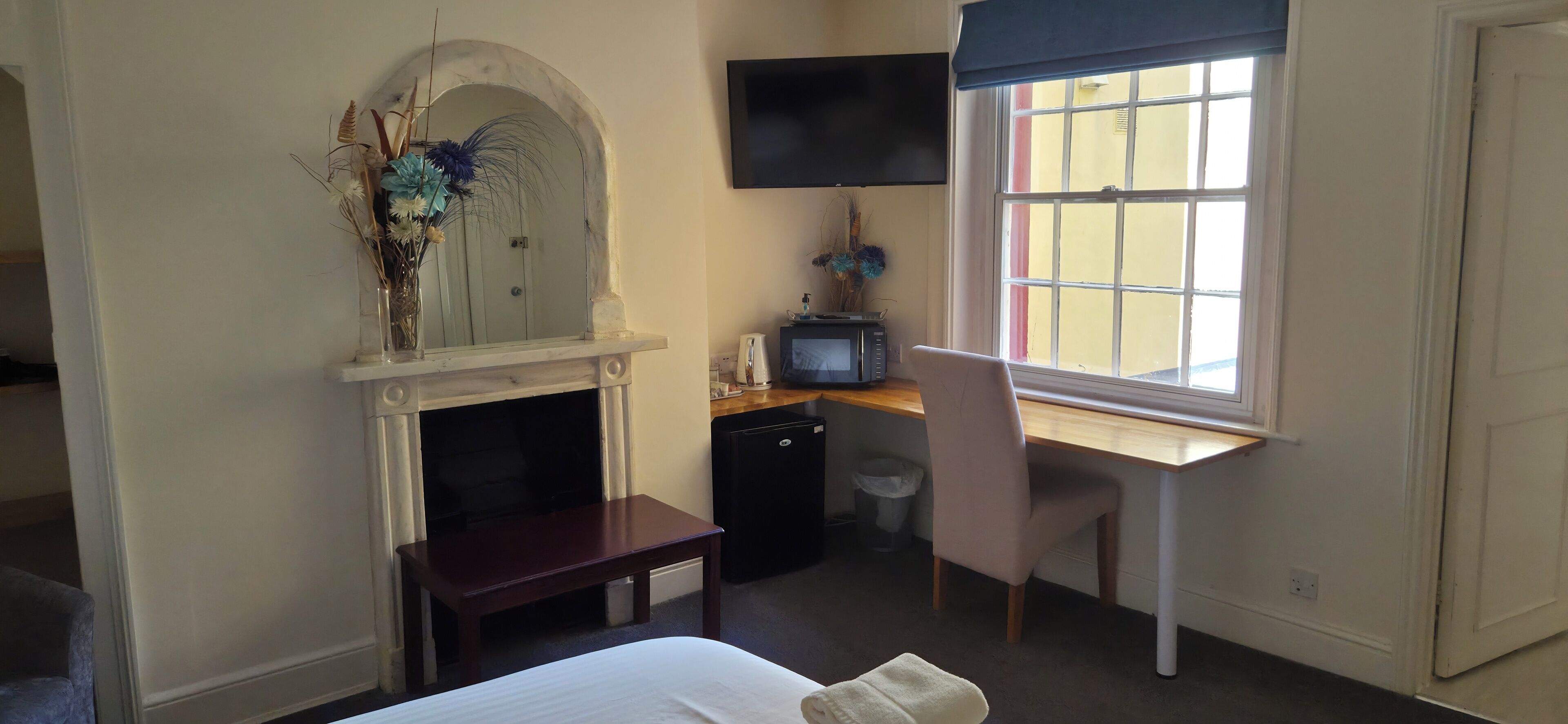 Ein Schlafzimmer mit einem Bett, einem Schreibtisch, einem Sessel, einem Fernseher, einem Kamin und einem Fenster mit Blick.