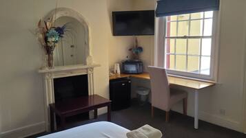 A bedroom with a bed, a desk, a chair, a television, a fireplace, and a window with a view.
