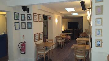 A dining area with wooden tables and chairs, framed pictures on the walls, and a fire extinguisher.