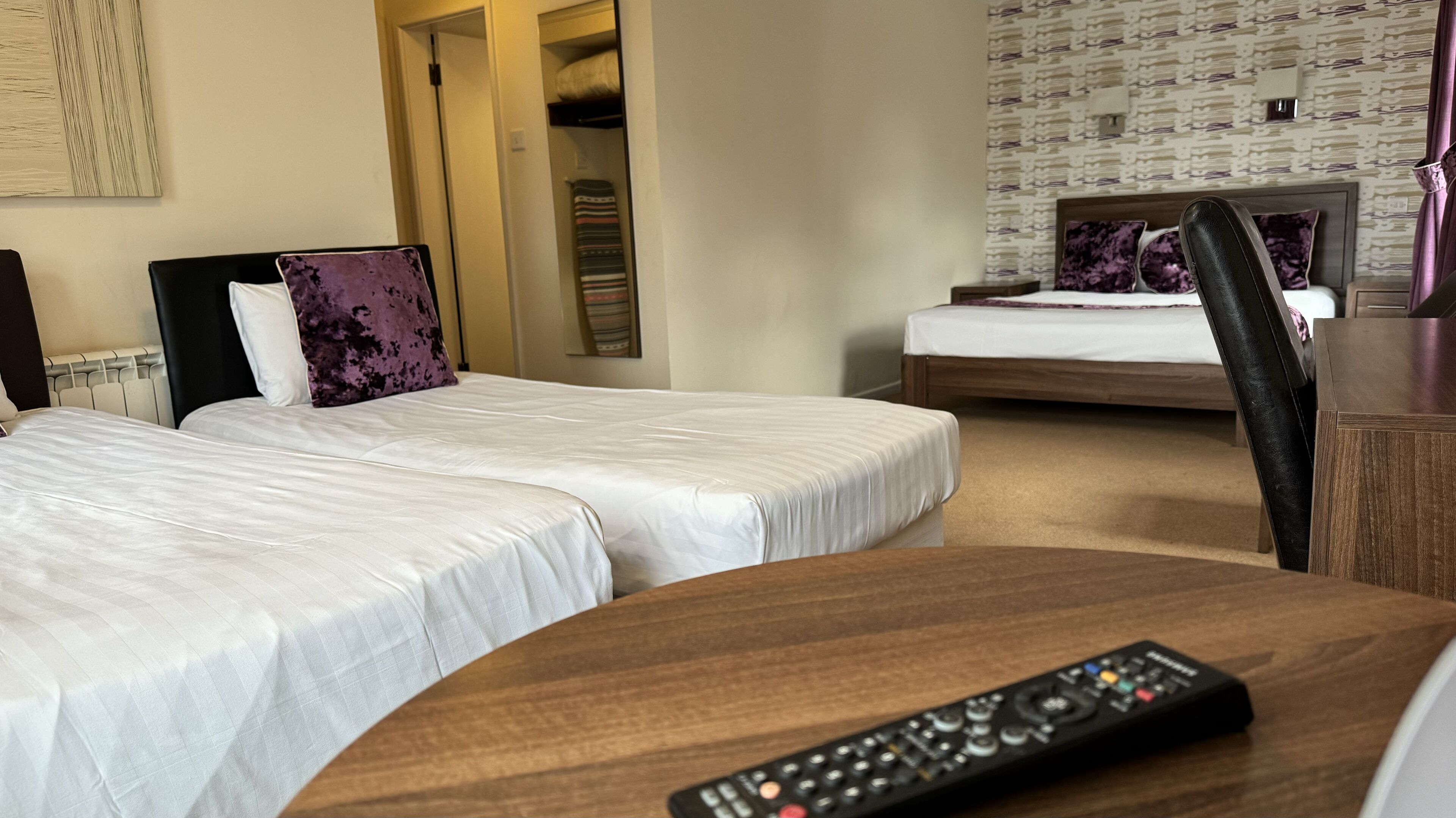 A hotel room with two beds, a wooden desk, and a remote control.