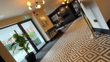 A hotel lobby with a patterned floor, a potted plant, a reception desk, and a chandelier.