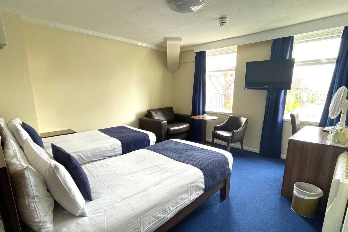 A hotel room with two beds, a desk, a chair, a TV, and a window with curtains.