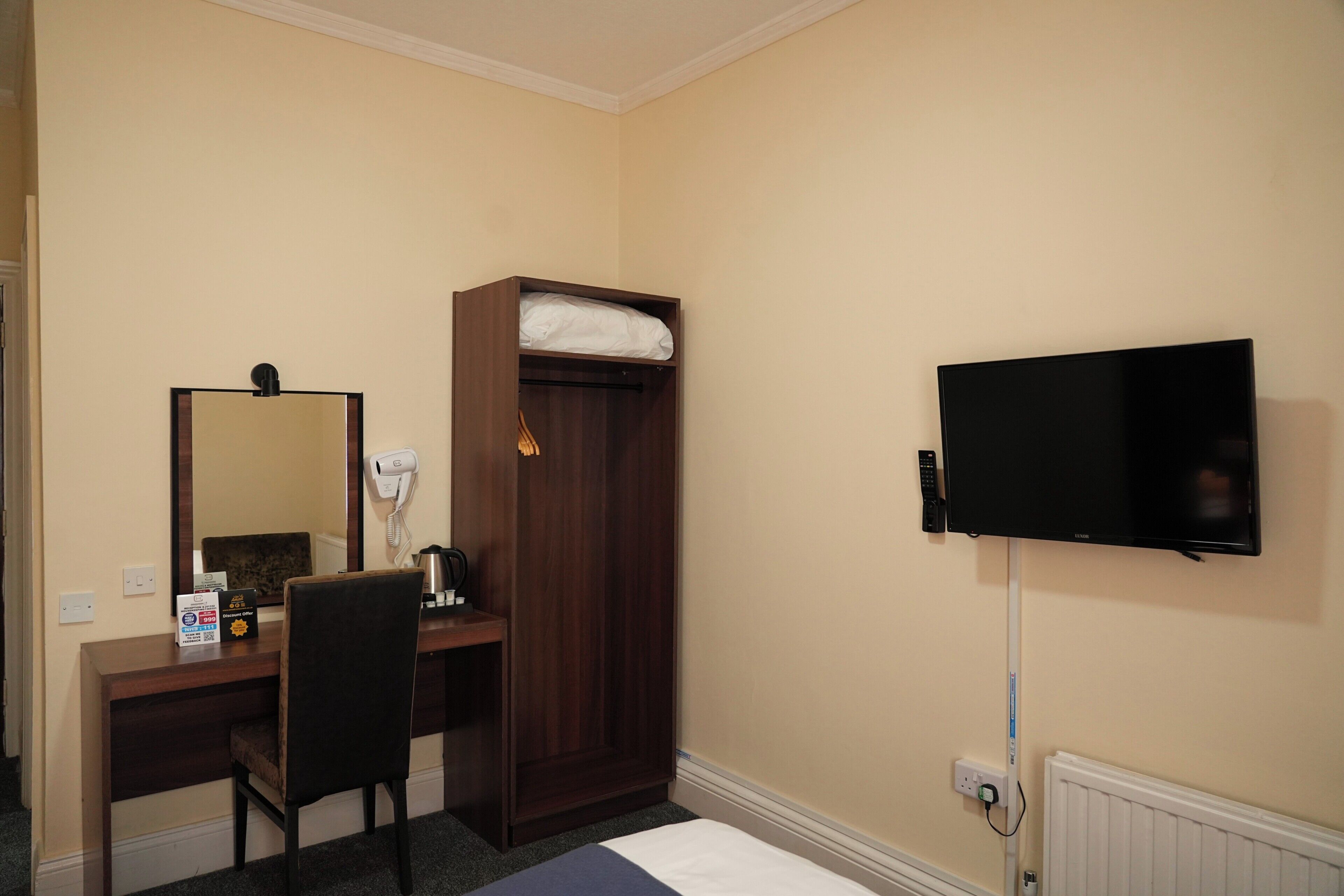 Camera d'albergo con scrivania, sedia, armadio, specchio, televisore e presa di corrente.