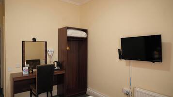 Camera d'albergo con scrivania, sedia, armadio, specchio, televisore e presa di corrente.