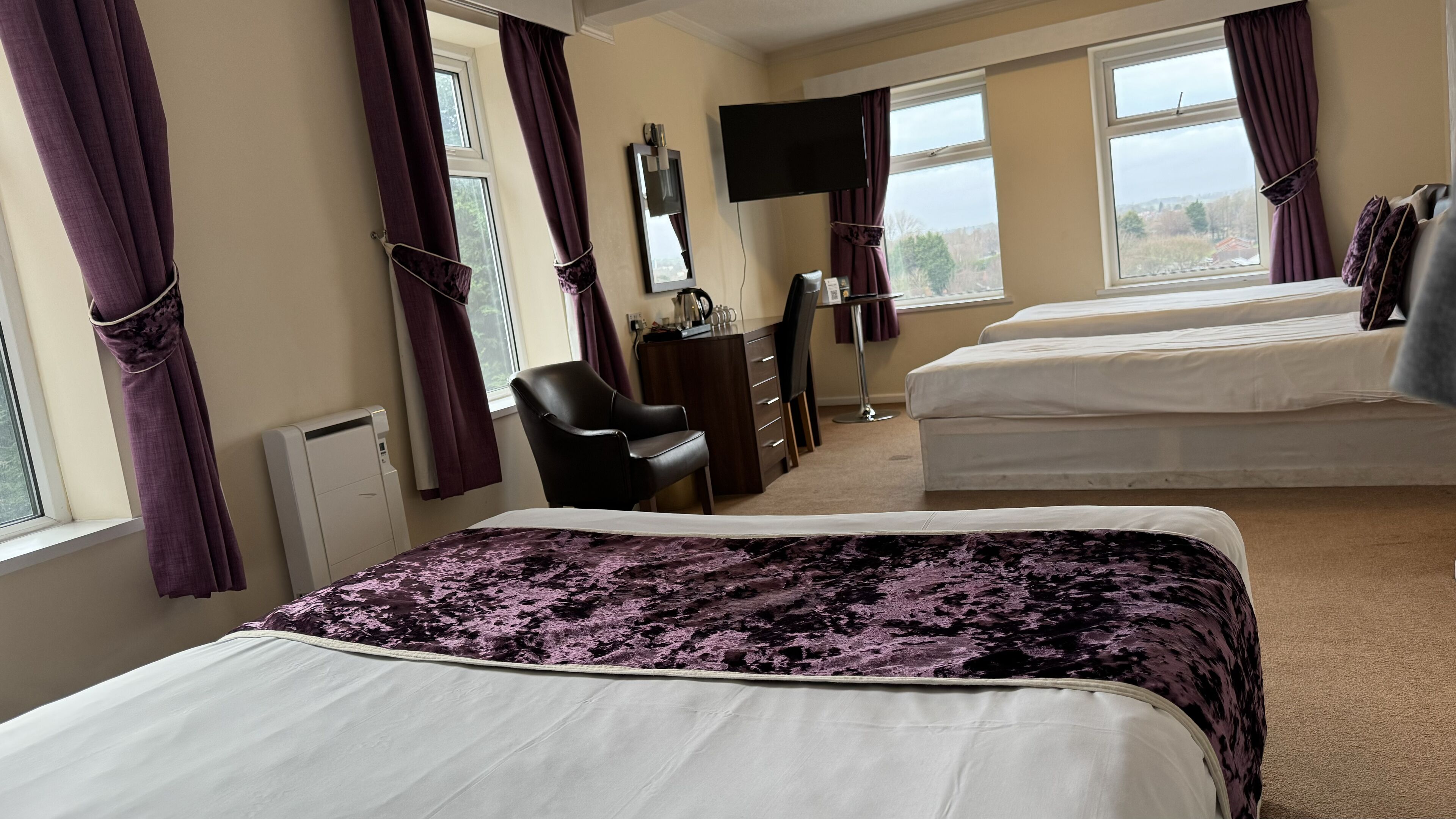 Habitación de hotel con dos camas, un escritorio, una silla, un televisor y vistas al exterior.