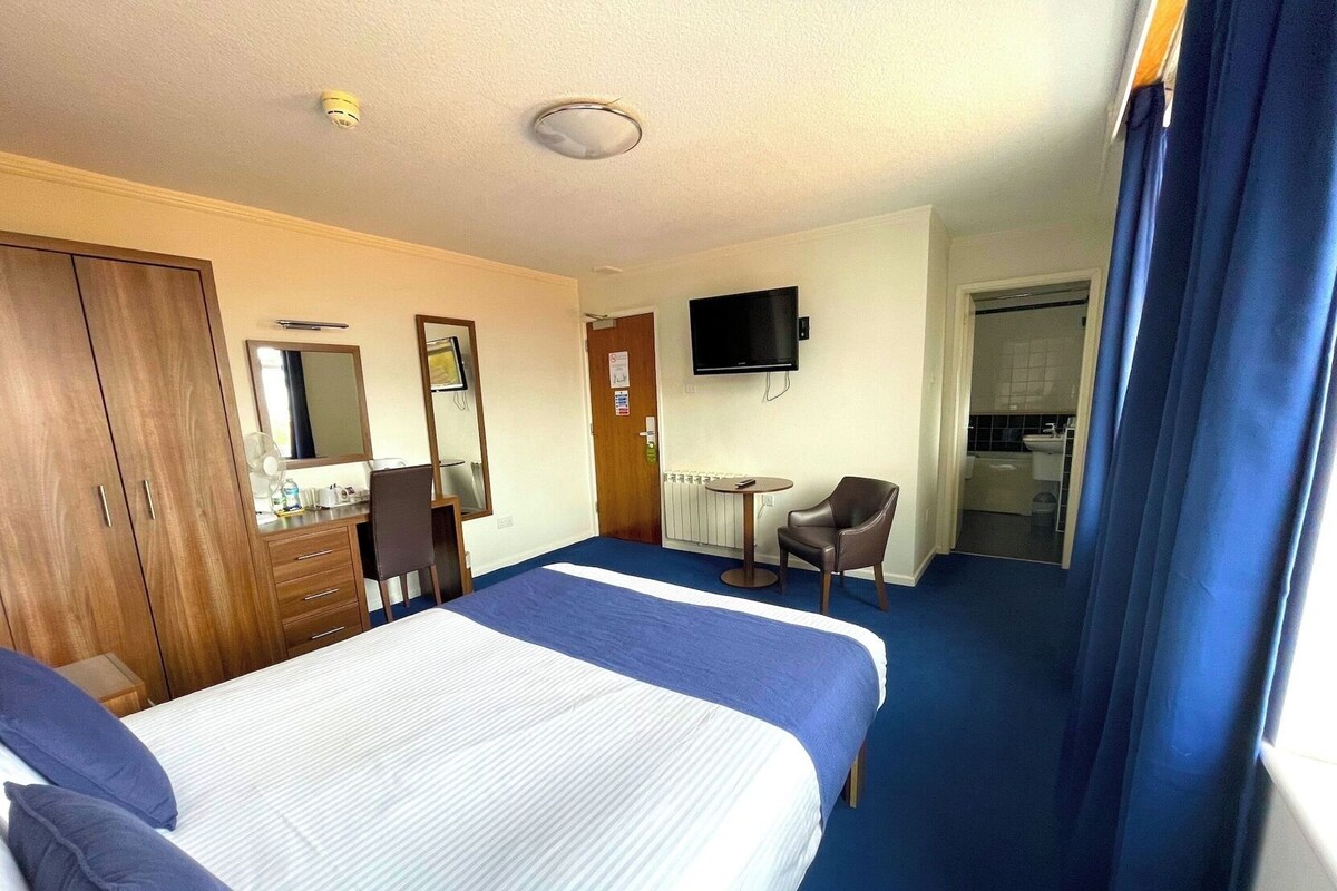 A hotel room with a bed, a desk, a chair, a television, and a bathroom.