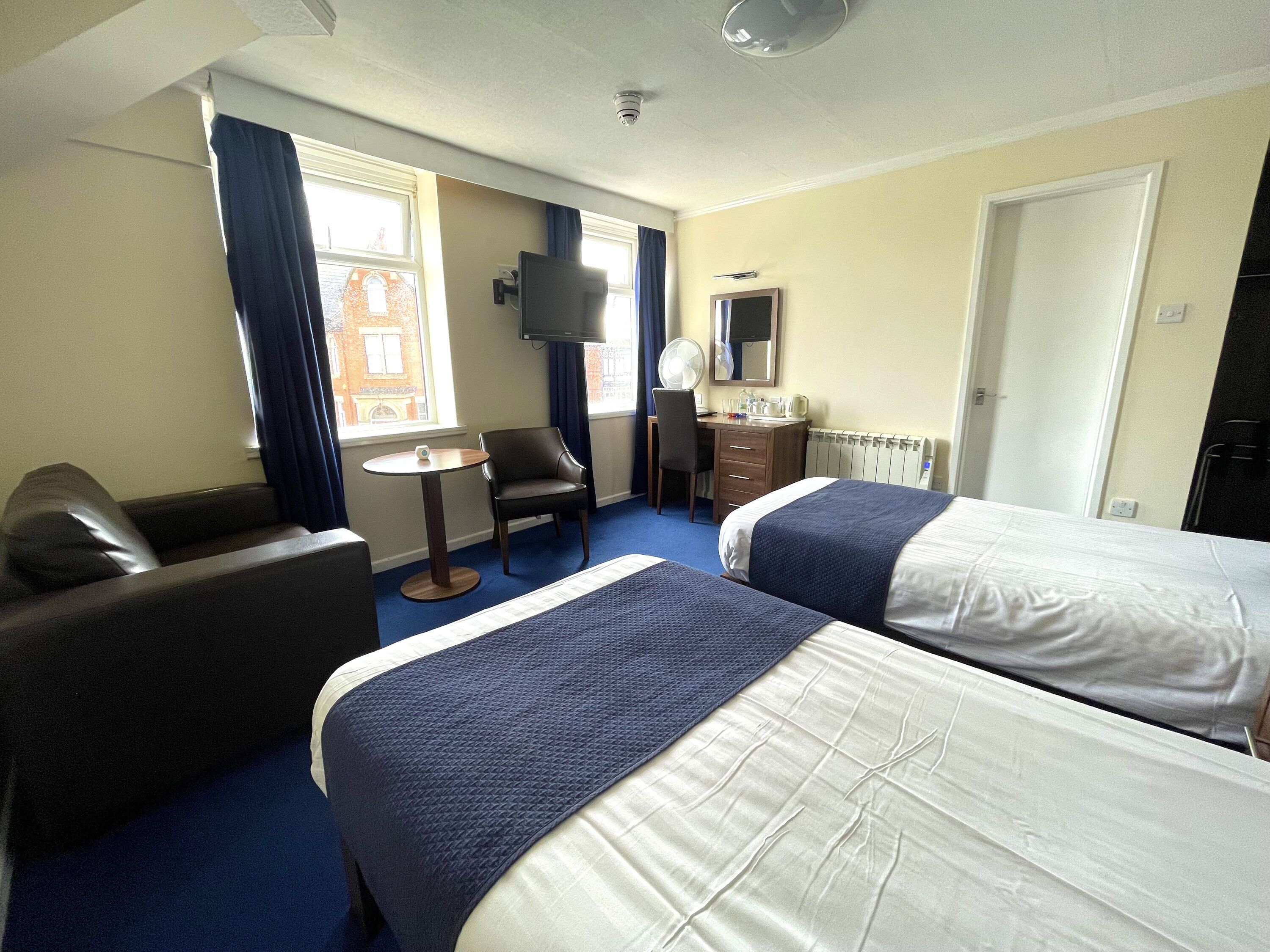 A hotel room with two beds, a desk, a chair, a TV, and a window with curtains.