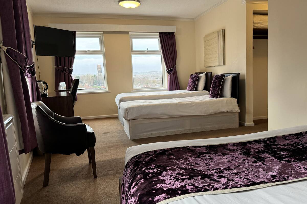 A hotel room with two beds, a TV, a desk, and a view of the city.