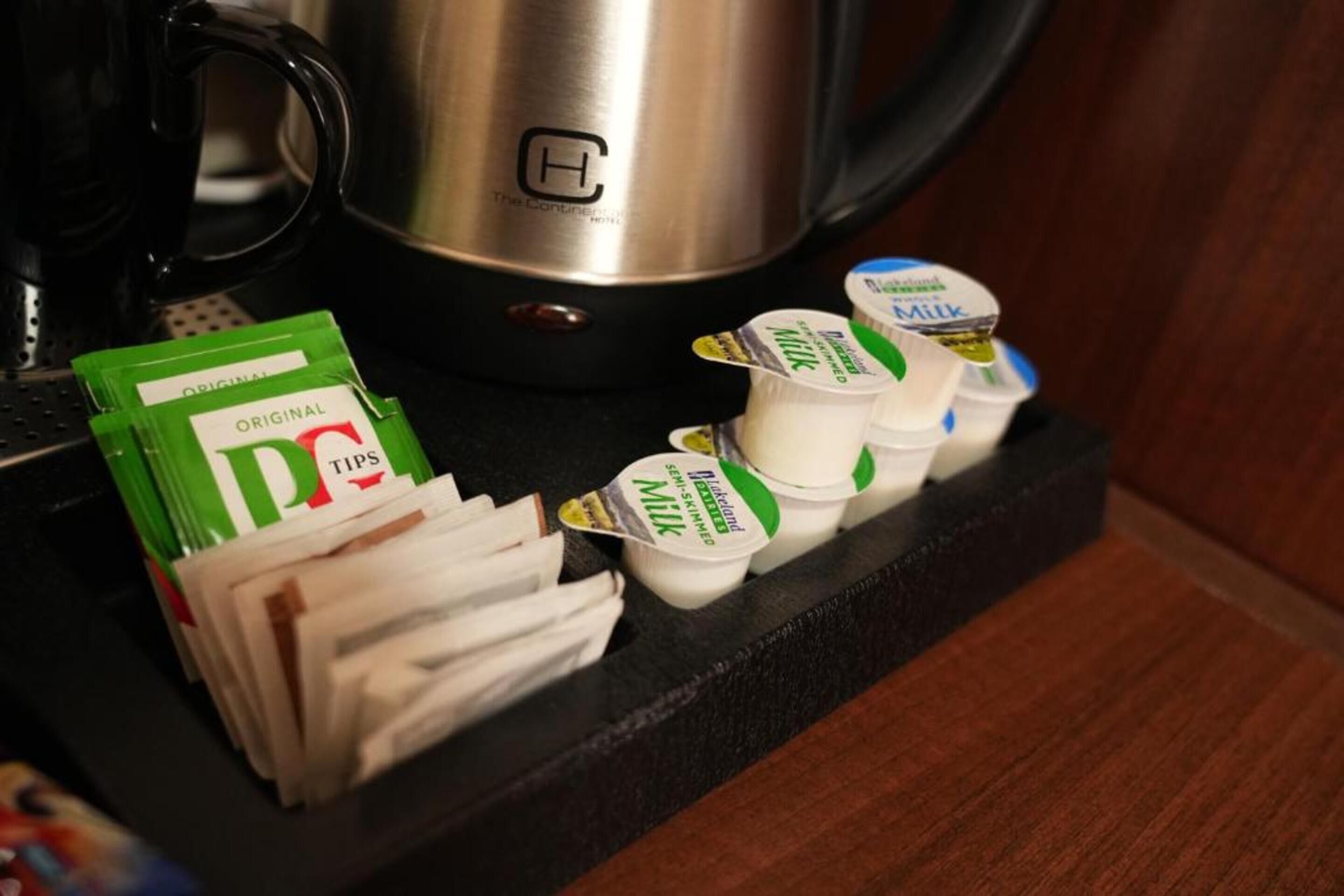 A kitchen counter with a coffee maker, a stainless steel kettle, and packets of coffee and milk.