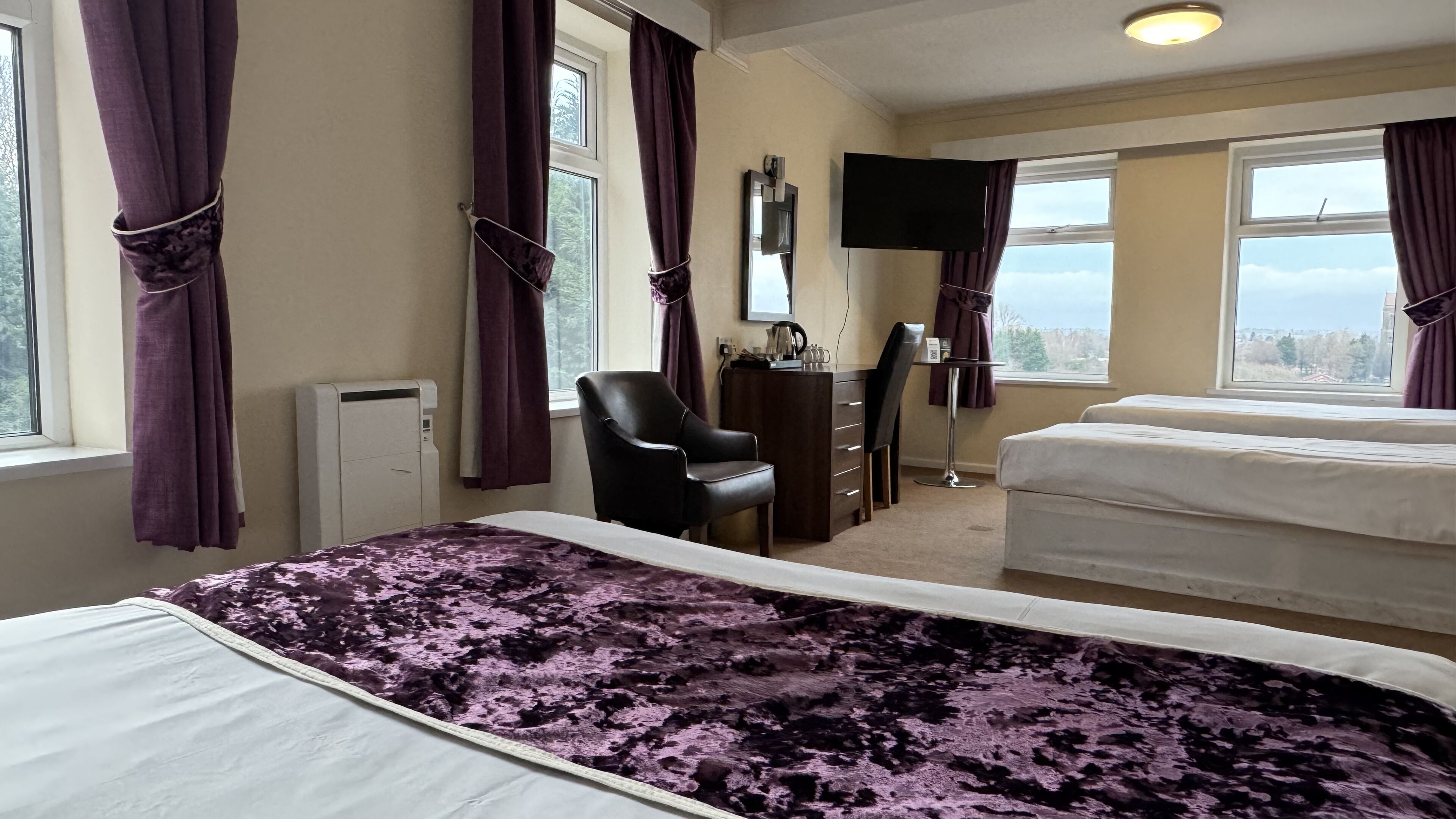 A hotel room with two beds, a chair, a dresser, a TV, and a window with a view.