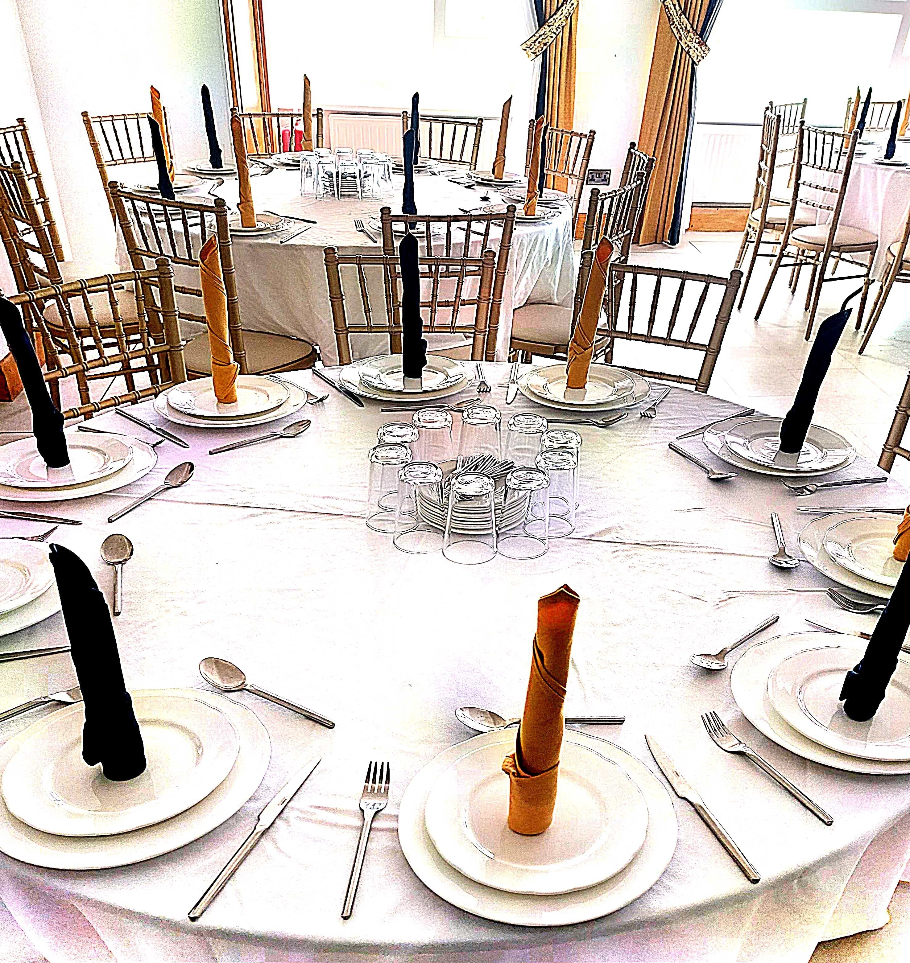 Une table ronde dressée pour un événement formel, avec plusieurs chaises, chacune agrémentée d’une serviette pliée et d’une bougie.