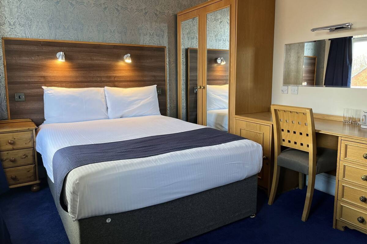 A hotel room with a bed, bedside tables, a desk, and a wardrobe.