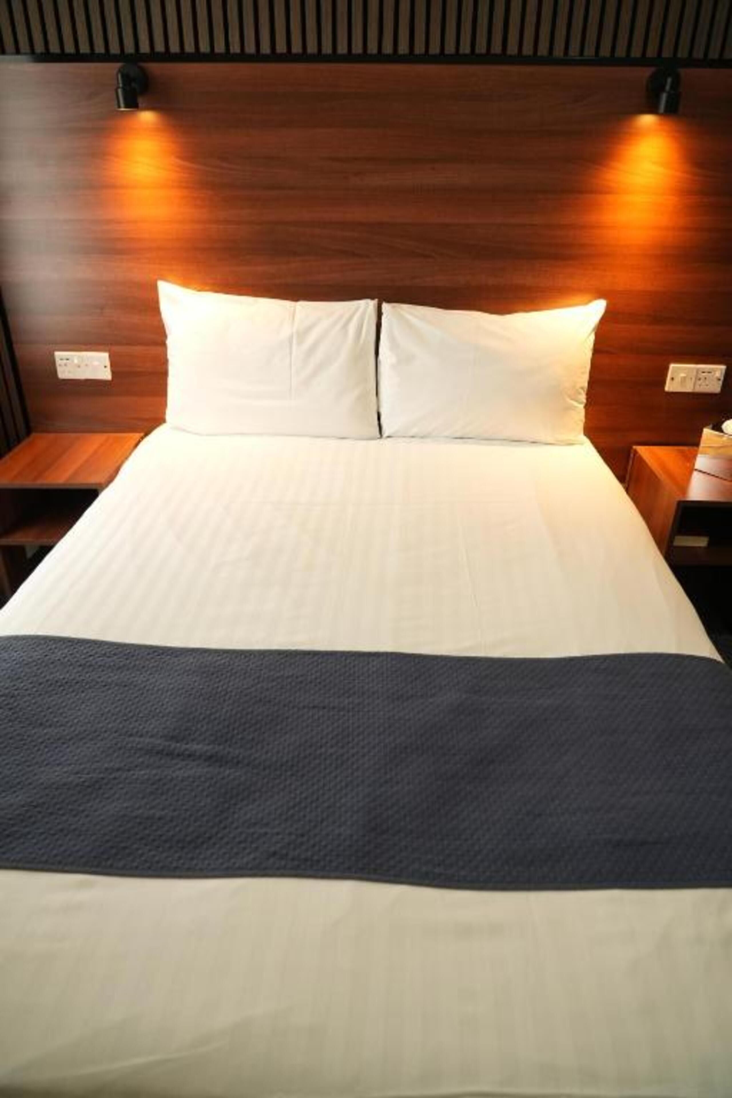 A neatly made bed with white linens and a dark blue blanket, flanked by wooden headboards and nightstands with lamps.