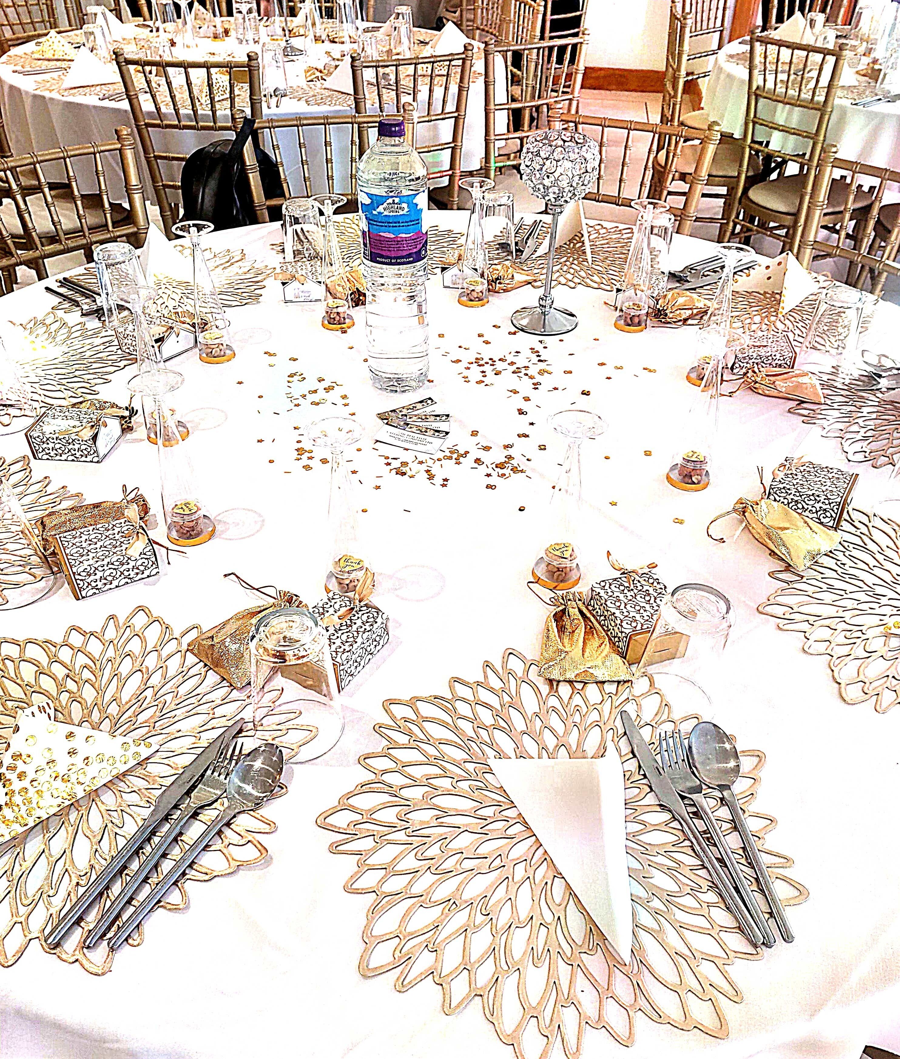 A round table set with cutlery, glassware, and decorative items, surrounded by chairs.