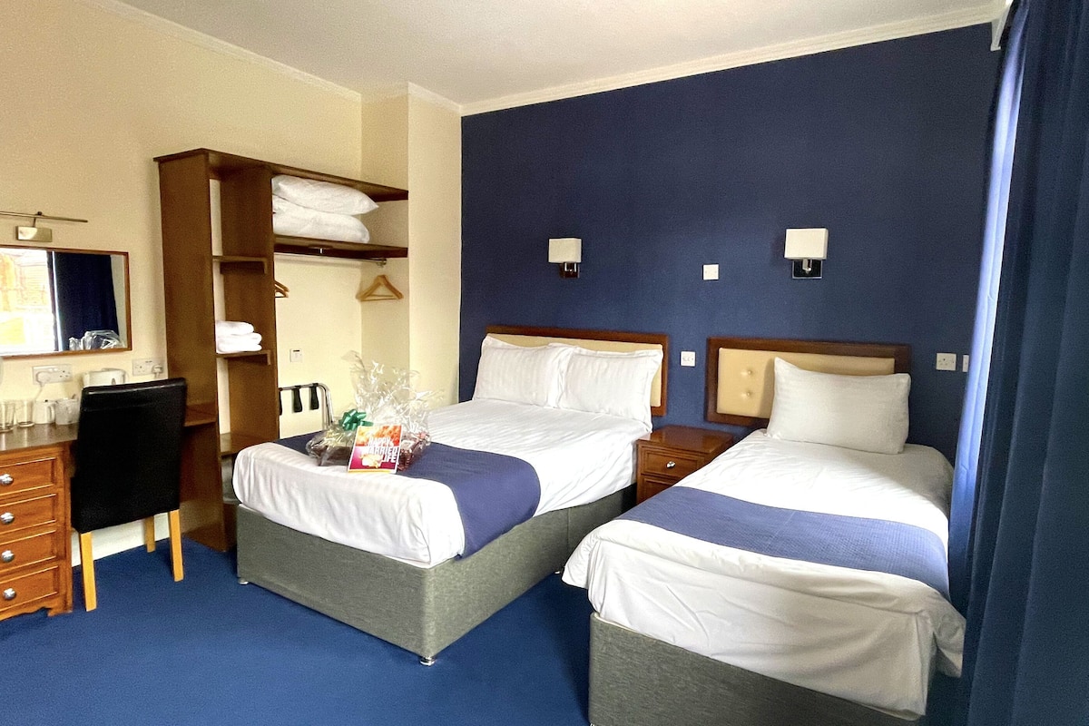A hotel room with two beds, a desk, a chair, a dresser, and a mirror.