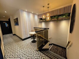A modern hotel lobby with a geometric patterned floor, a staircase with a glass railing, and a wall-mounted plant.