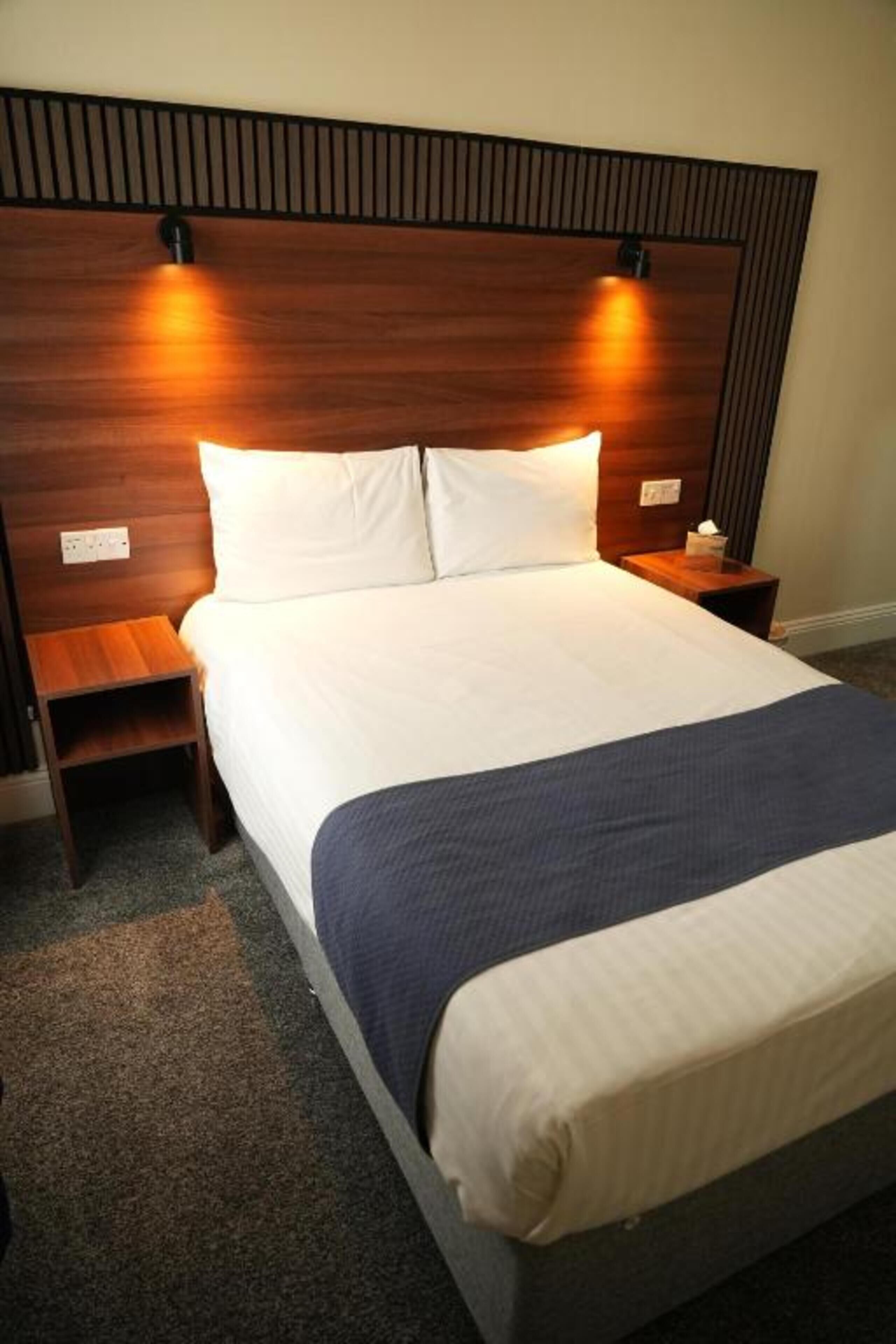 A hotel room with a large bed, wooden headboard, bedside tables, and a carpeted floor.