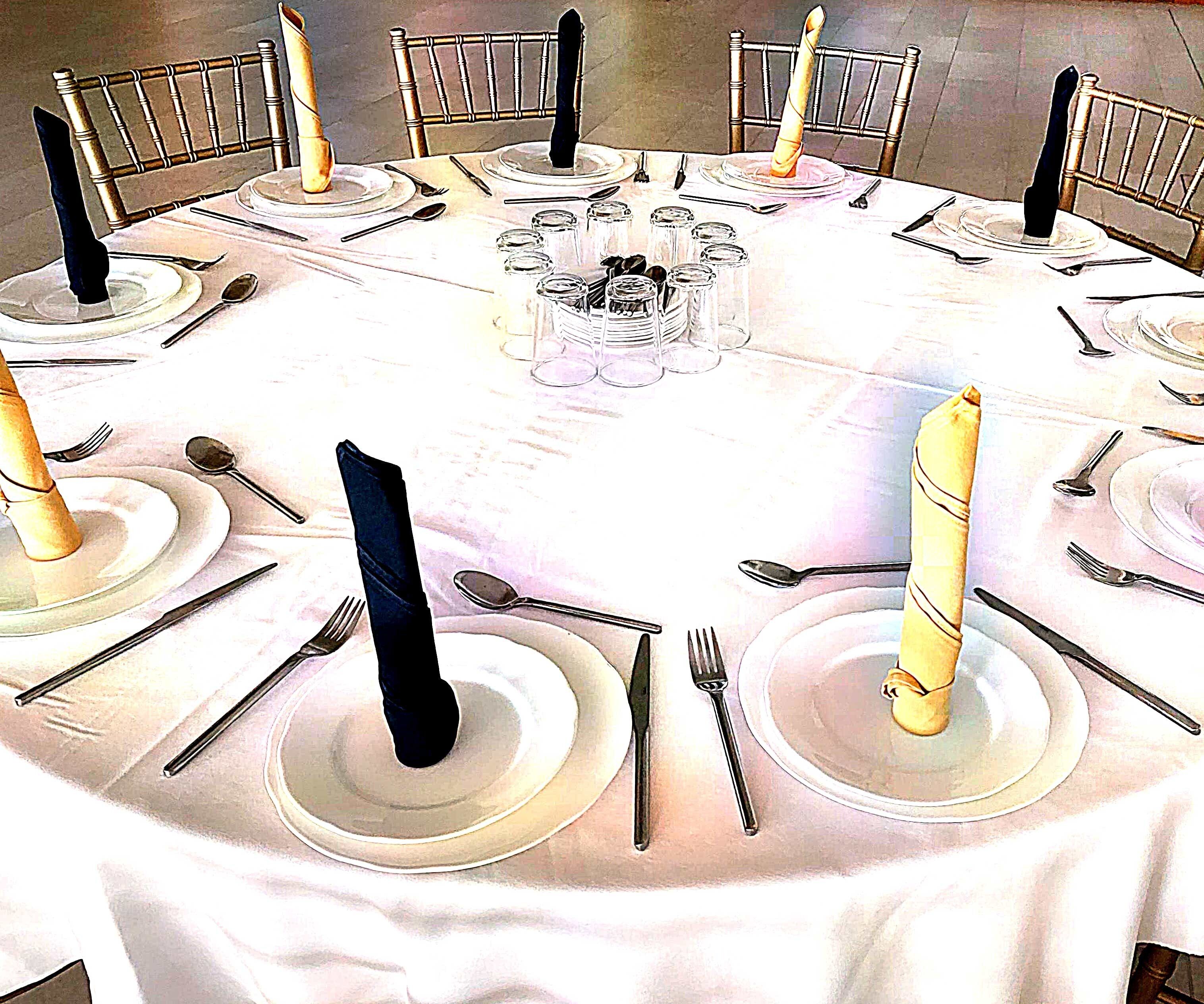 Una mesa redonda dispuesta para una cena formal, con varios puestos, copas y velas.