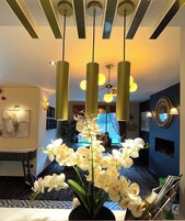 Un moderno vestíbulo de hotel con una gran planta de orquídea, iluminación colgante y una pared de acento azul.