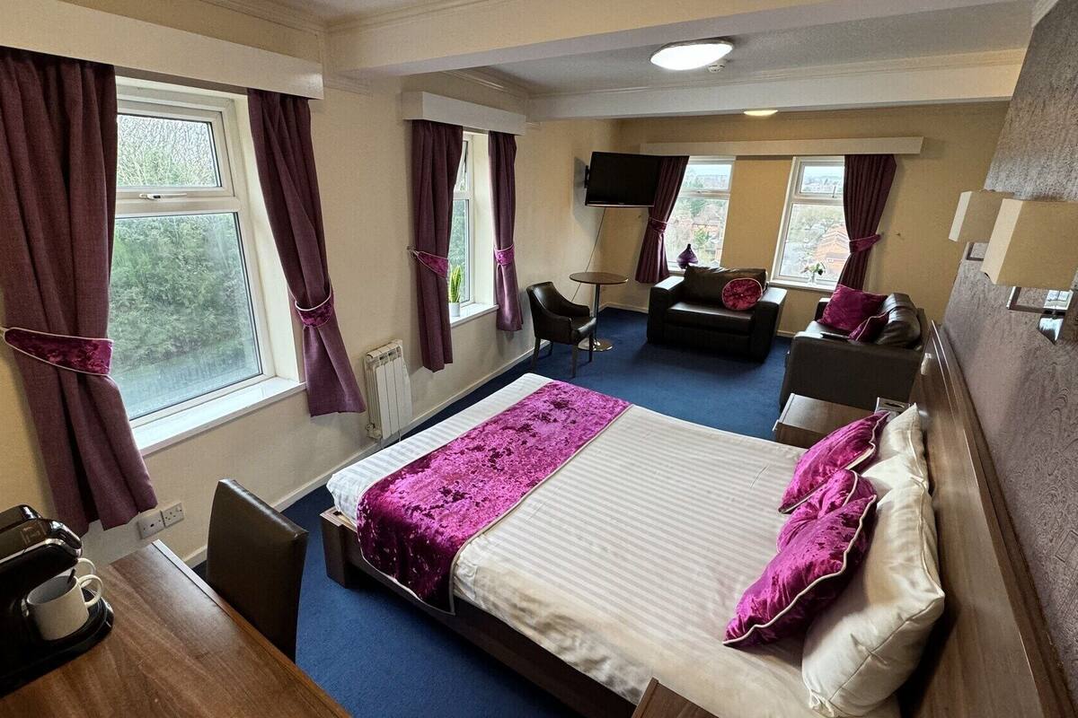 A hotel room with a bed, a desk, a chair, a sofa, a TV, and a window with curtains.