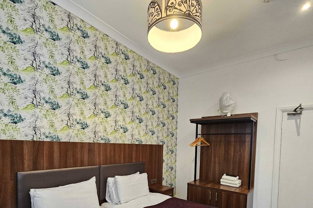 A hotel room with a large bed, a wooden headboard, a wardrobe, and a hanging light fixture.