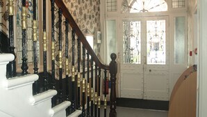 A grand staircase with ornate black and gold railings, a chandelier, and a white door with decorative glass panels. - Chelsea House Hotel (London)