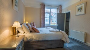 A bedroom with a bed, bedside table, lamp, and a view of a building through the window. - The Rosscourt - Adults only (Bournemouth)