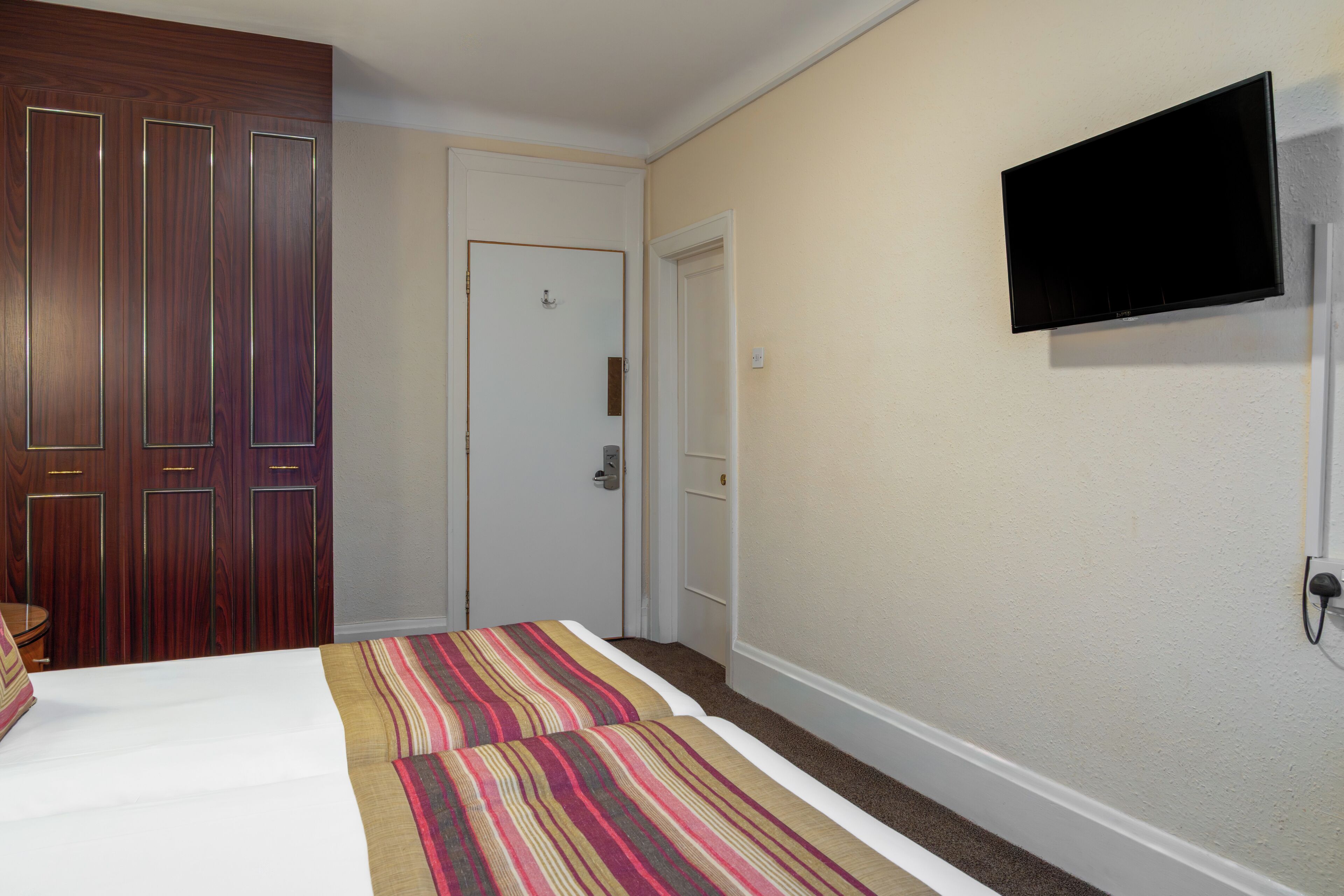 A hotel room with a bed, a television mounted on the wall, and a door.
